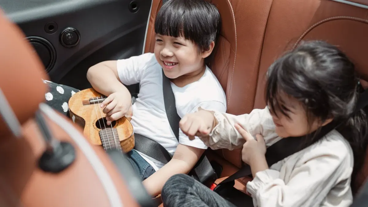 A dog sitting in the back seat of a car wearing a harness clipped to the seat belt buckle