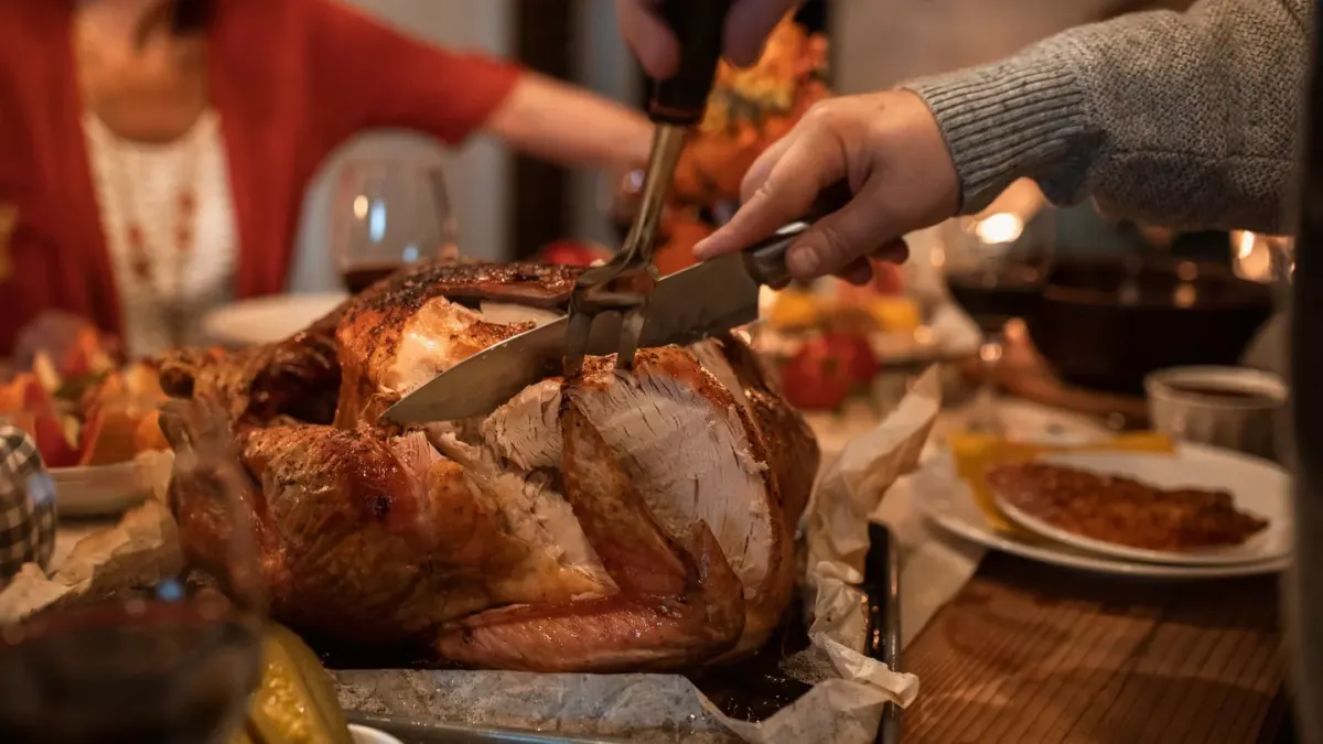 A dog sitting near a table with a roasted turkey, looking up expectantly