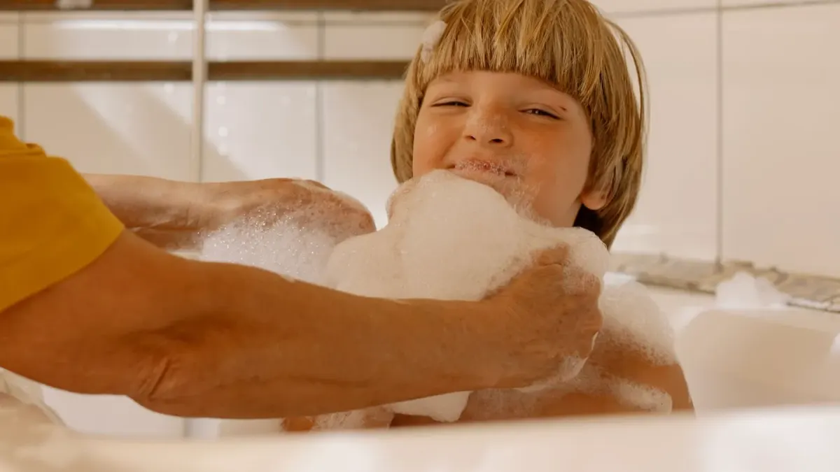 A dog standing in a bathtub covered in shampoo lather during a bath