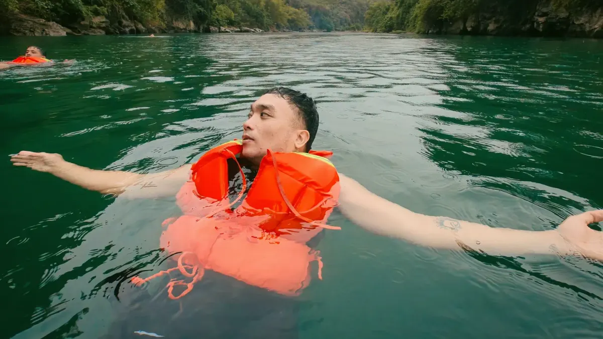 A dog wearing an orange flotation vest swimming near a dock