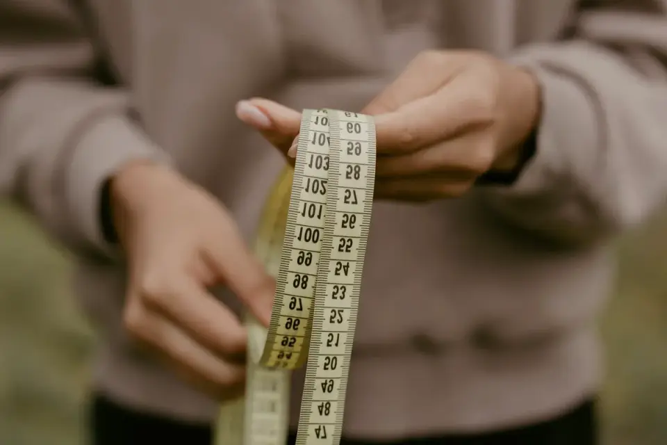 A person kneeling to measure a dog's shoulder height with a soft tape measure