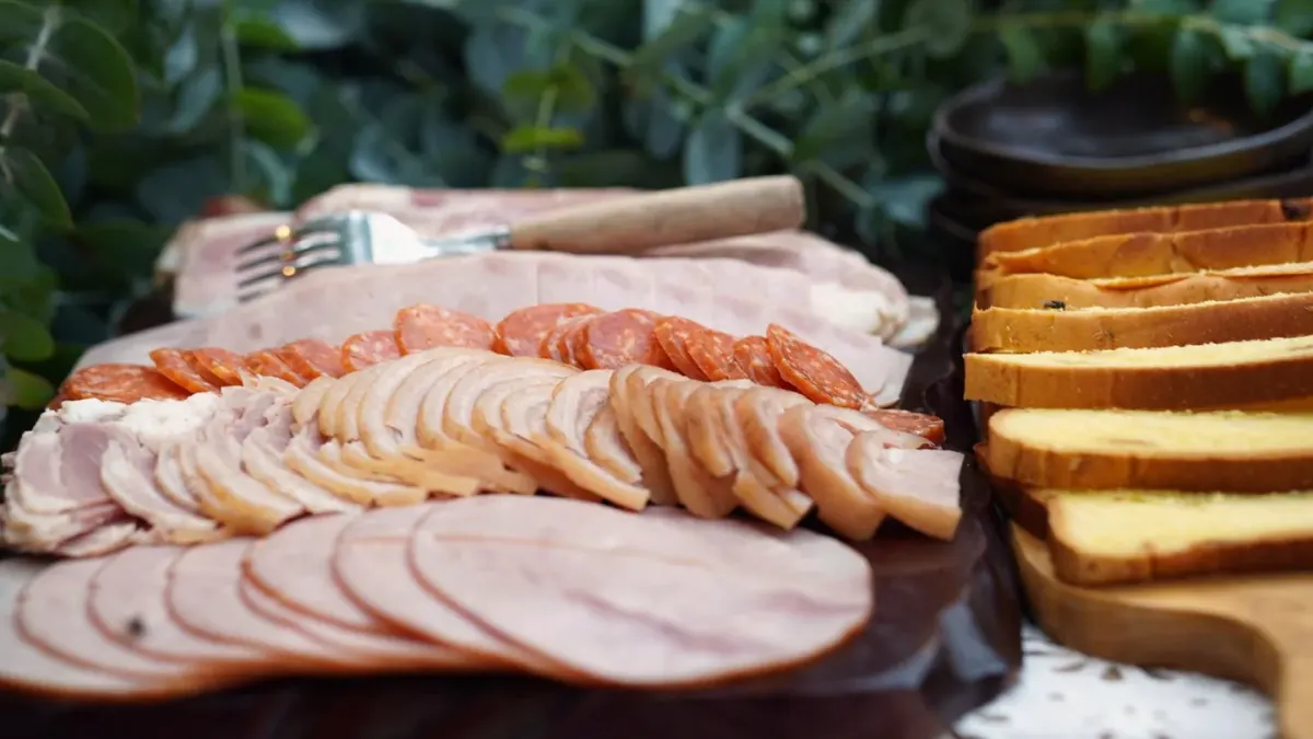 A plate of sliced ham on a kitchen counter with a dog looking up nearby