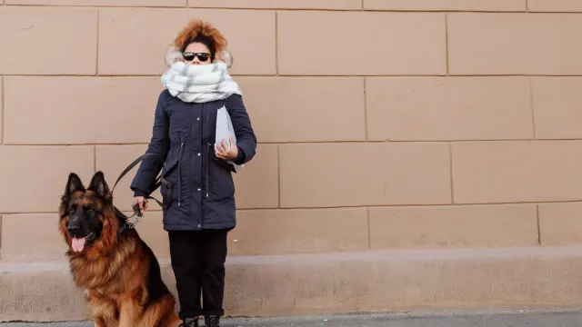 A woman crouches to work with a leashed dog outside a training building