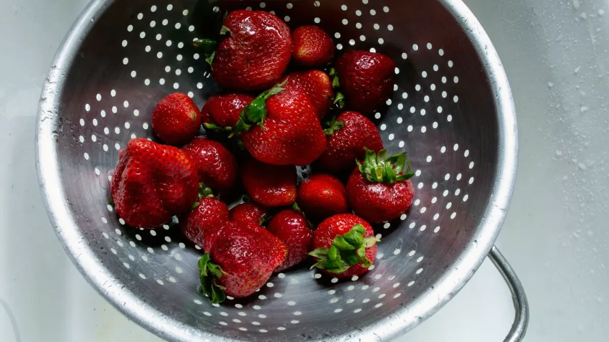 Fresh whole strawberries next to a dog's stainless steel bowl on a kitchen counter