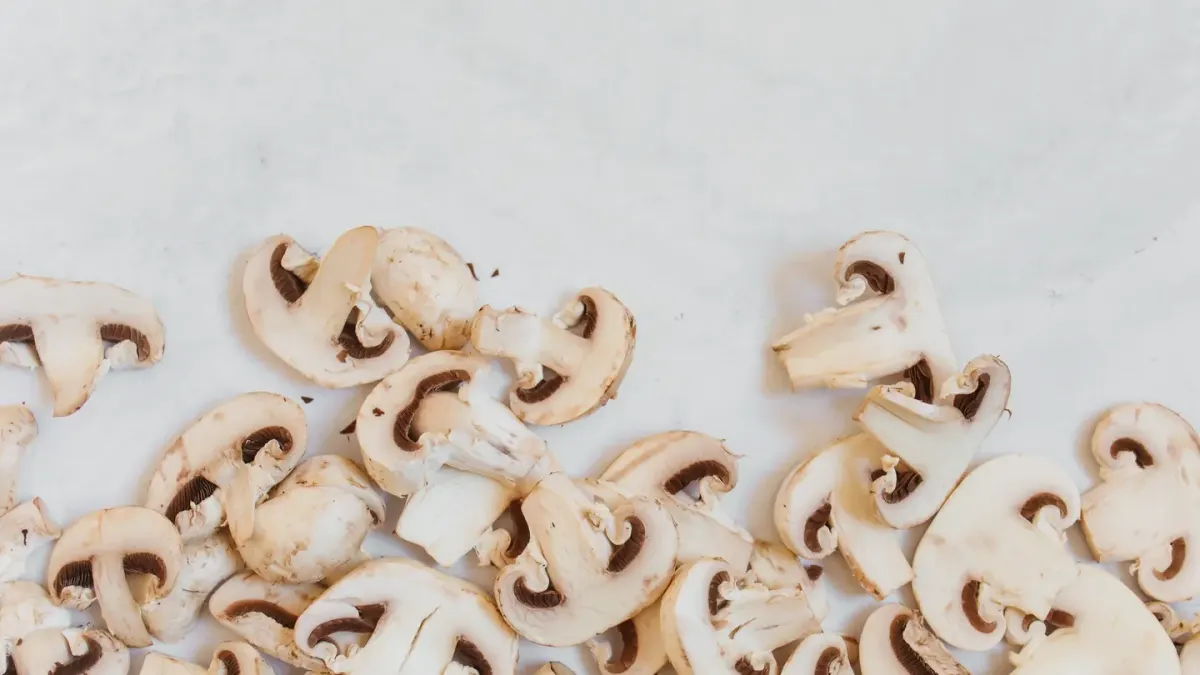 Sliced white button mushrooms on a cutting board with a dog looking on nearby