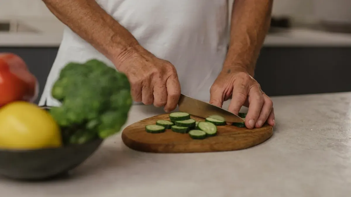 Small dog sitting on a kitchen floor near a cutting board scattered with broccoli florets